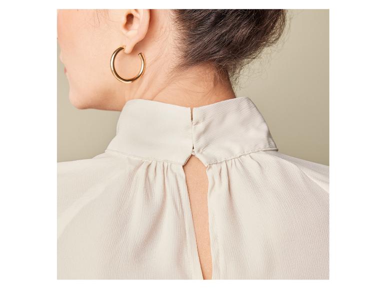 Žena má na sebe bielu blúzku s otvoreným chrbtom.