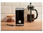 Čierny elektrický mlynček na kávu, french press a nádoba s mletou kávou na drevenej doske.