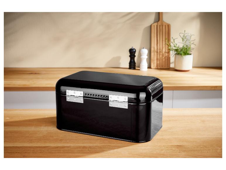 Čierna kovová nádoba na chlieb na drevenom stole v kuchyni.