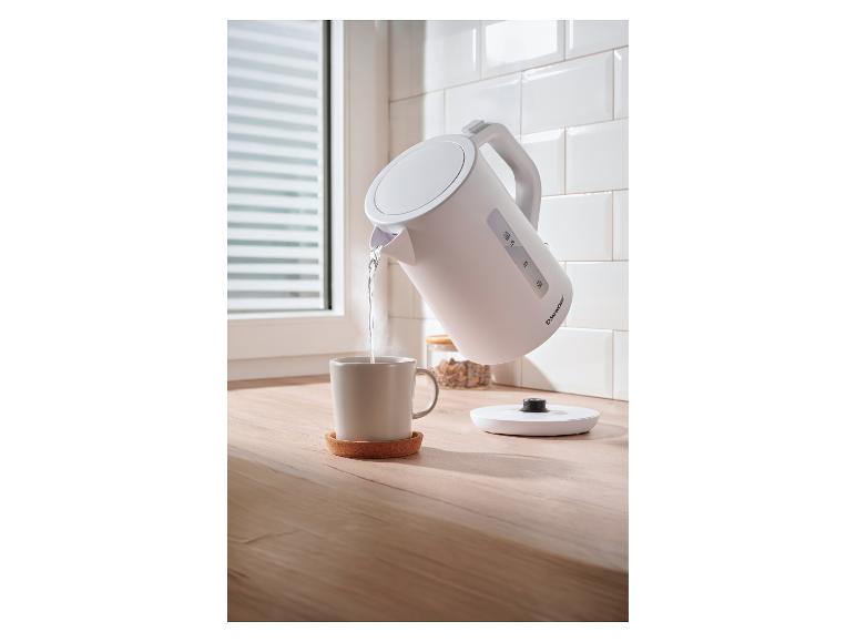 Rýchlovarná kanvica SilverCrest nalieva horúcu vodu do hrnčeka na drevenej doske.