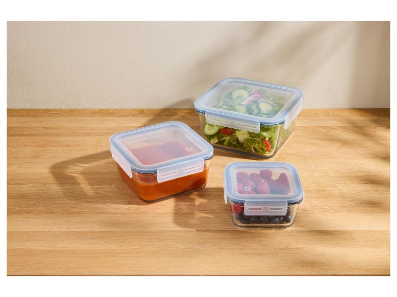 Tri sklenené nádoby na jedlo s modrými viečkami, plné šalátu, omáčky a bobúľ, na drevenom stole.