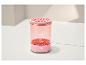 Ružové kozmetické zariadenie s priehľadným telom, vzorovaným vrchom a tlačidlom napájania.