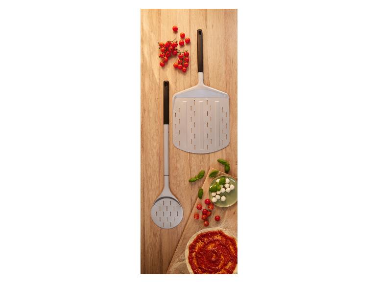Lopaty na pizzu s cherry paradajkami, mozzarellou, bazalkou a základom na pizzu na drevenej doske.