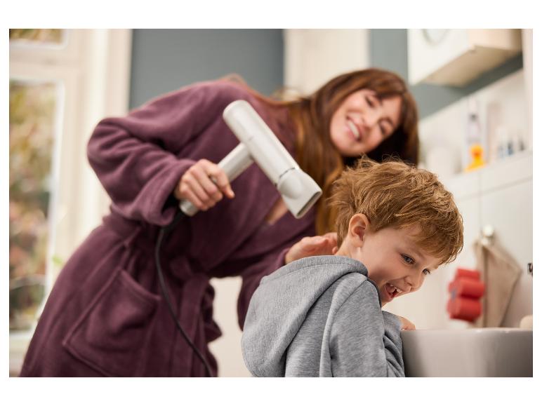 Žena suší chlapcovi vlasy fénom.