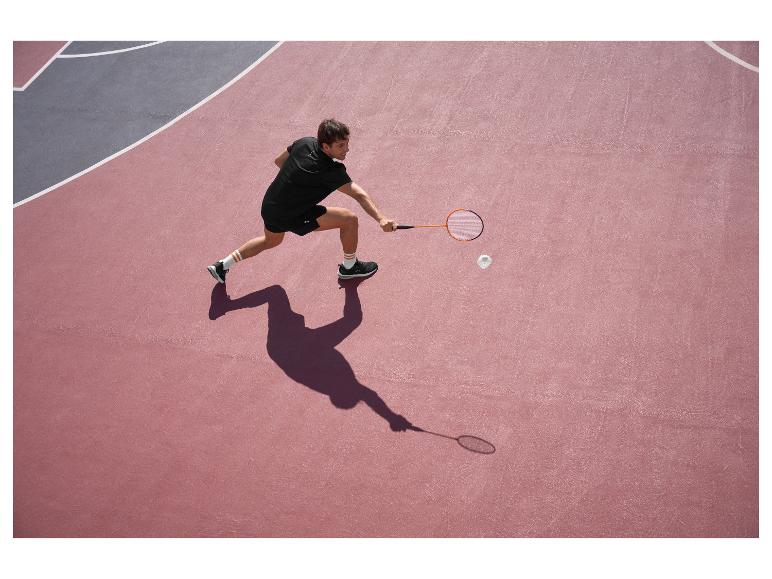 Muž v čiernom hrá bedminton na ružovo-sivom kurte.