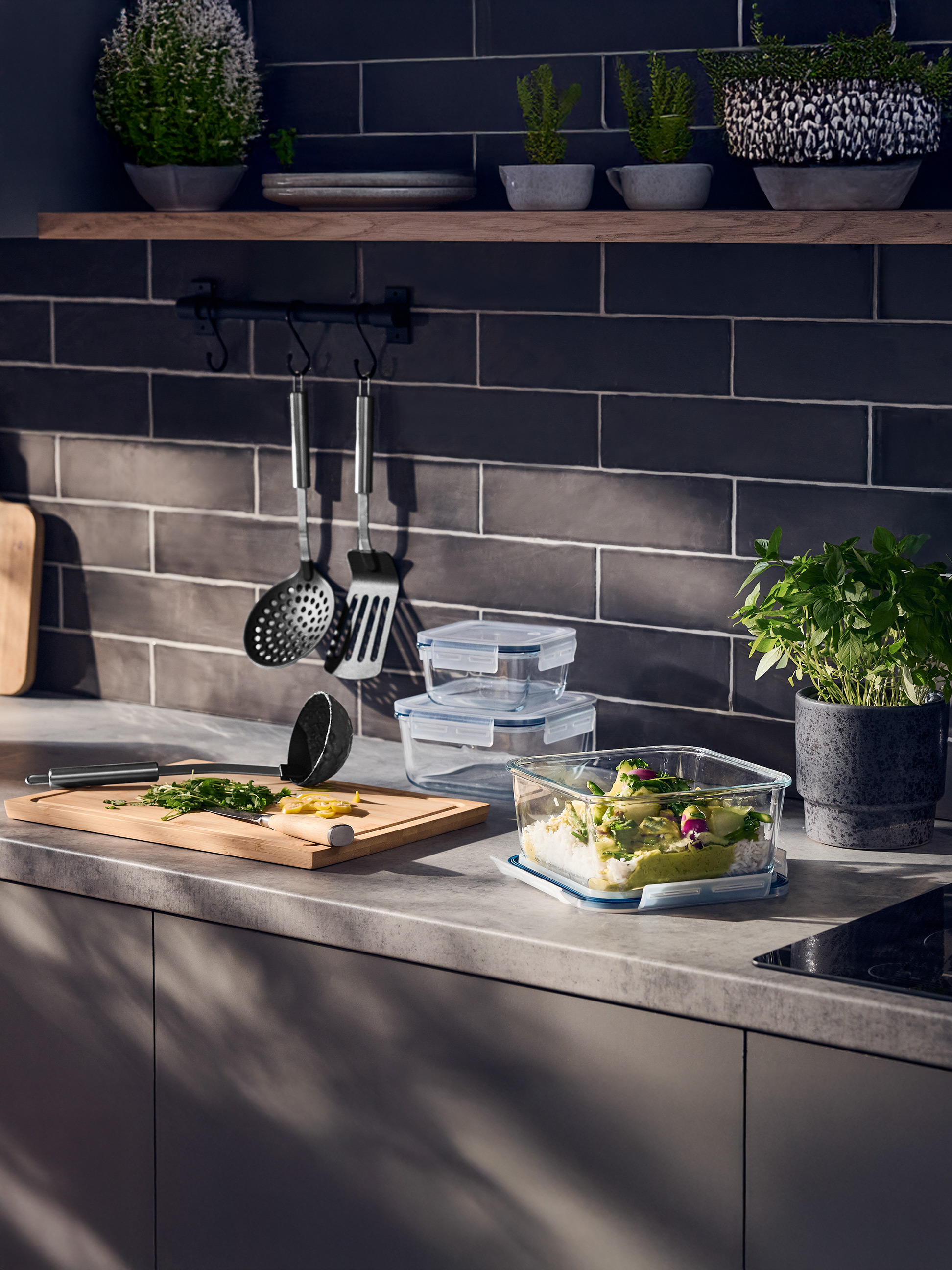 Kuchynská linka so sklenenými nádobami na potraviny, doskou na krájanie a bylinkami.