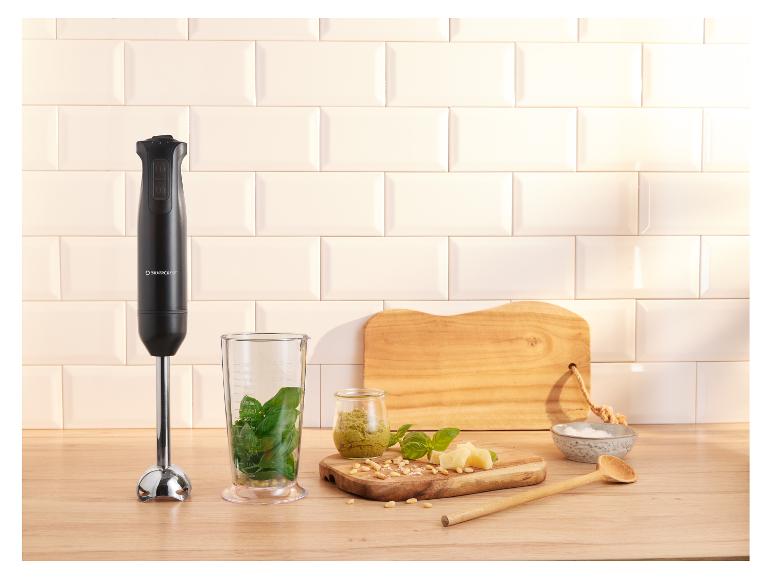Ponorný mixér s prísadami na pesto na drevenej doske.