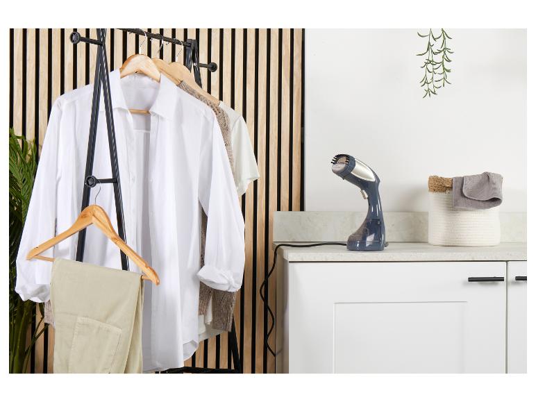 Naparovač odevov na pracovnej doske vedľa vešiaka na oblečenie s košeľami a nohavicami.