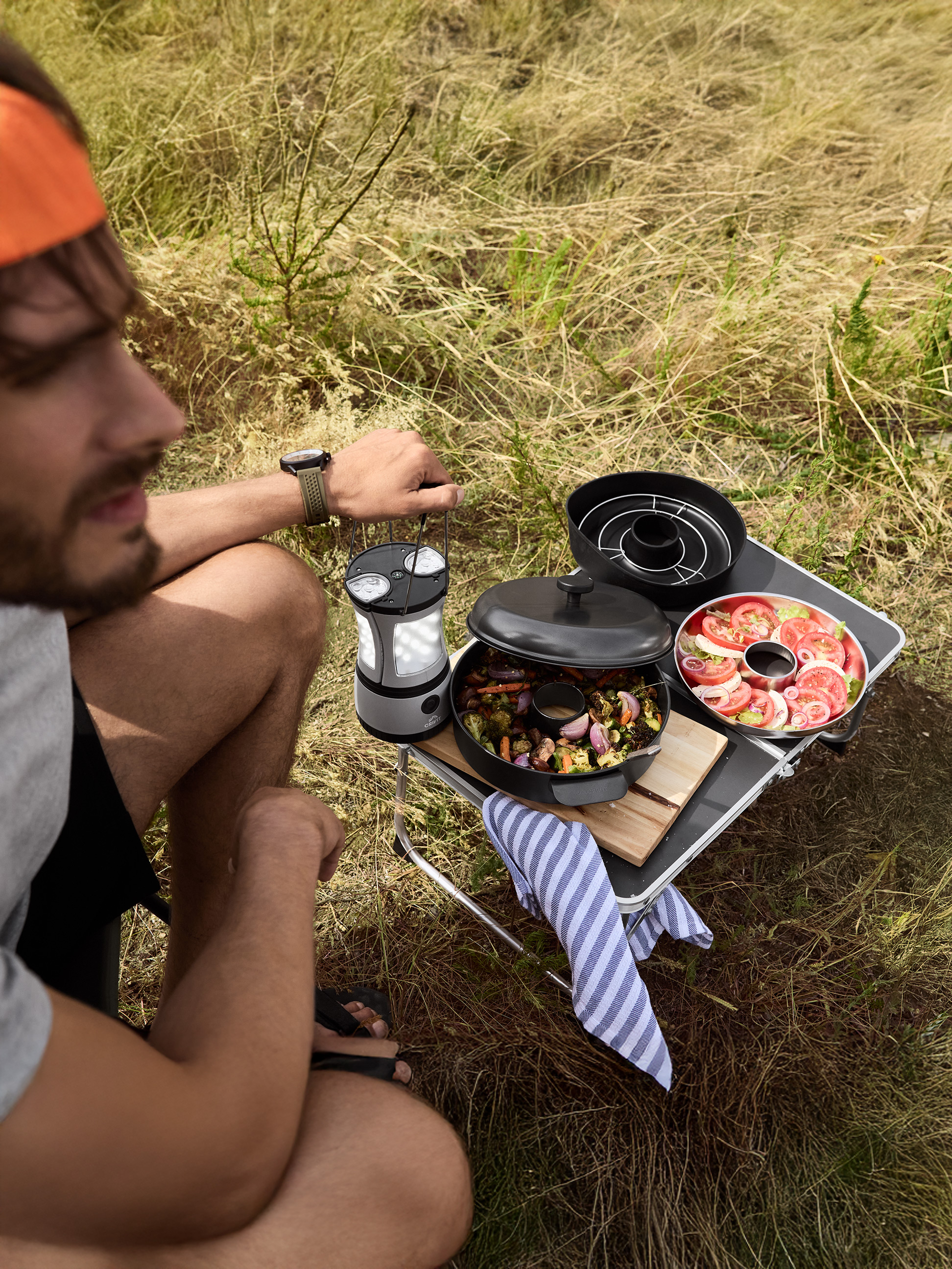 Muž varí vonku s prenosným grilom, podáva pečenú zeleninu a paradajkový šalát.