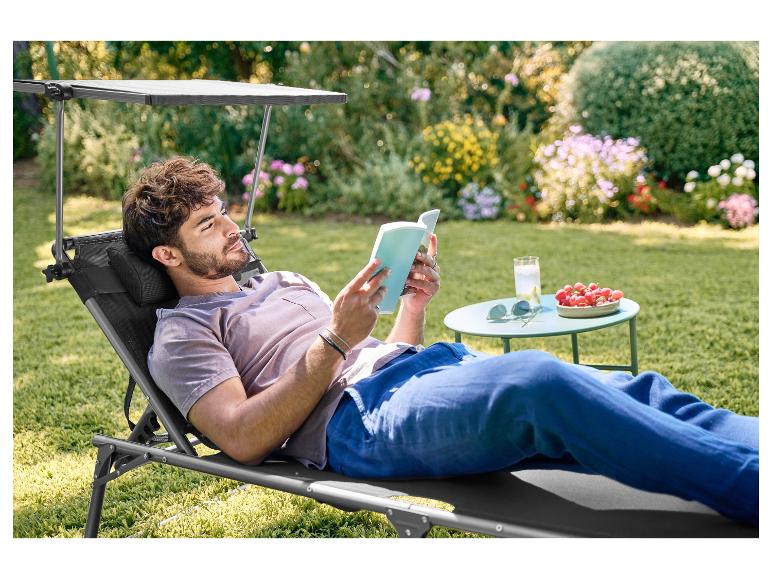 Muž relaxuje na záhradnom ležadle s tienidlom, číta knihu v záhrade.