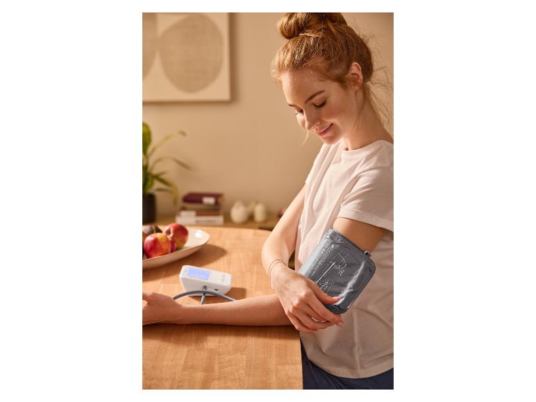 Žena si doma meria krvný tlak tlakomerom.