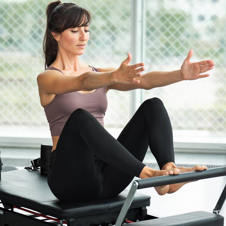 Žena cvičiaca Pilates na reformeri, v tope a čiernych legínach.