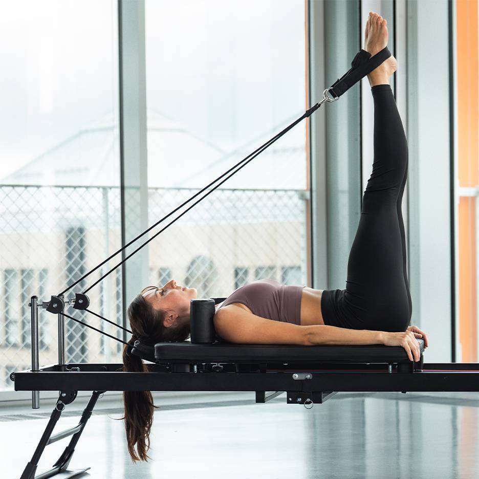 Žena cvičiaca nohy na pilates reformer stroji.
