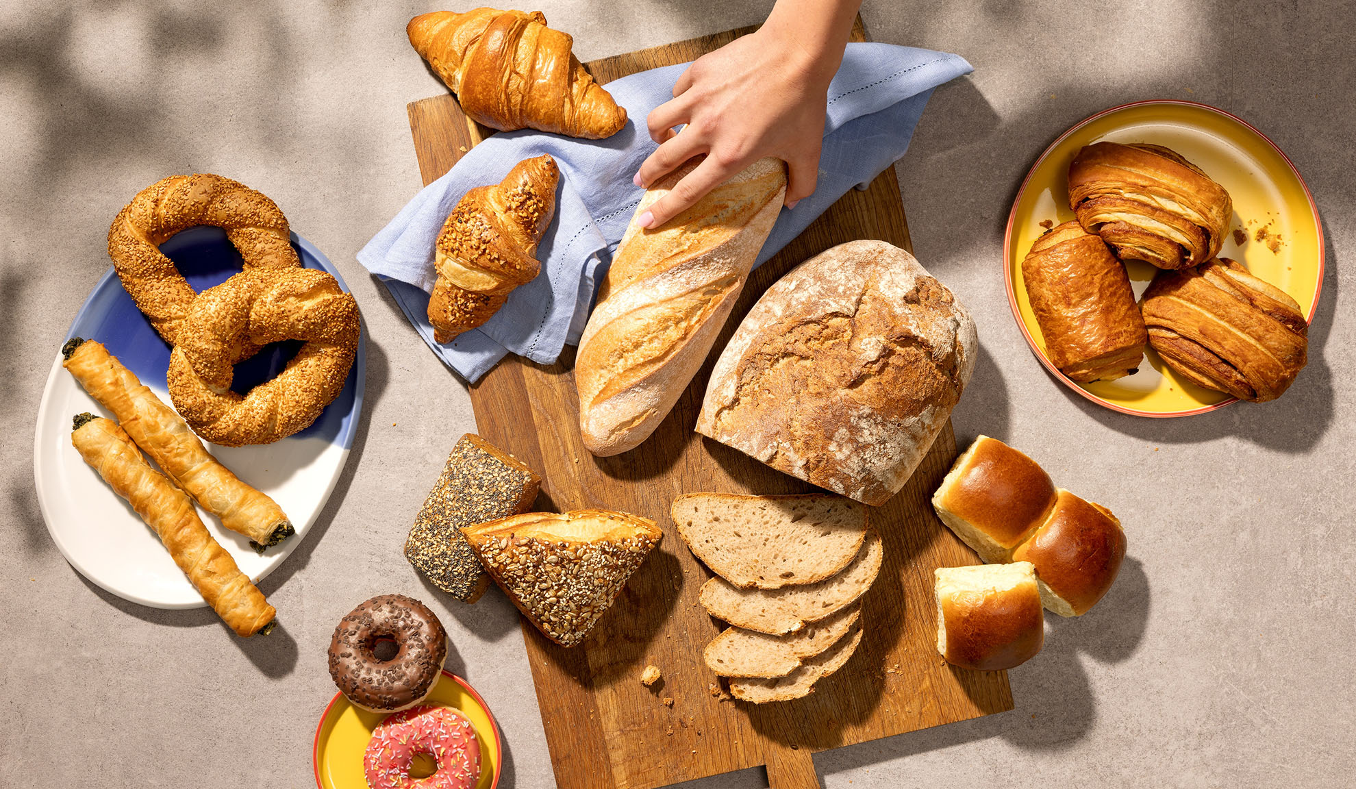 Sortiment čerstvého pečiva vrátane chleba, croissantov, pečiva a šišiek na stole.