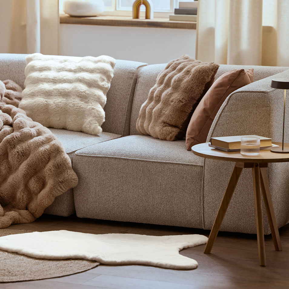 Sivá modulárna pohovka s nadýchanými vankúšmi a prikrývkami, vedľa konferenčného stolíka.