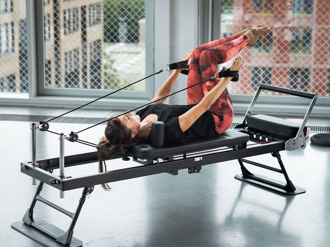 Žena cvičiaca Pilates na reformeri v červených jogových legínach.