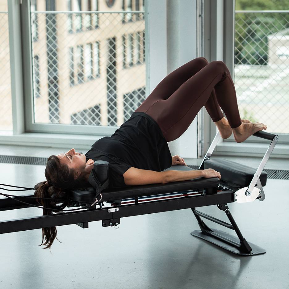 Žena cvičí Pilates na reformer stroji, nohy hore.
