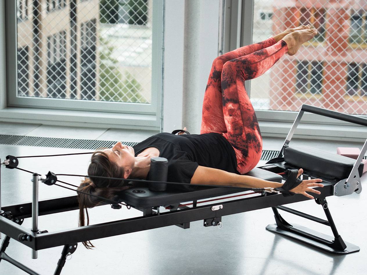 Žena cvičí Pilates na reformeri, v červeno-čiernych legínach