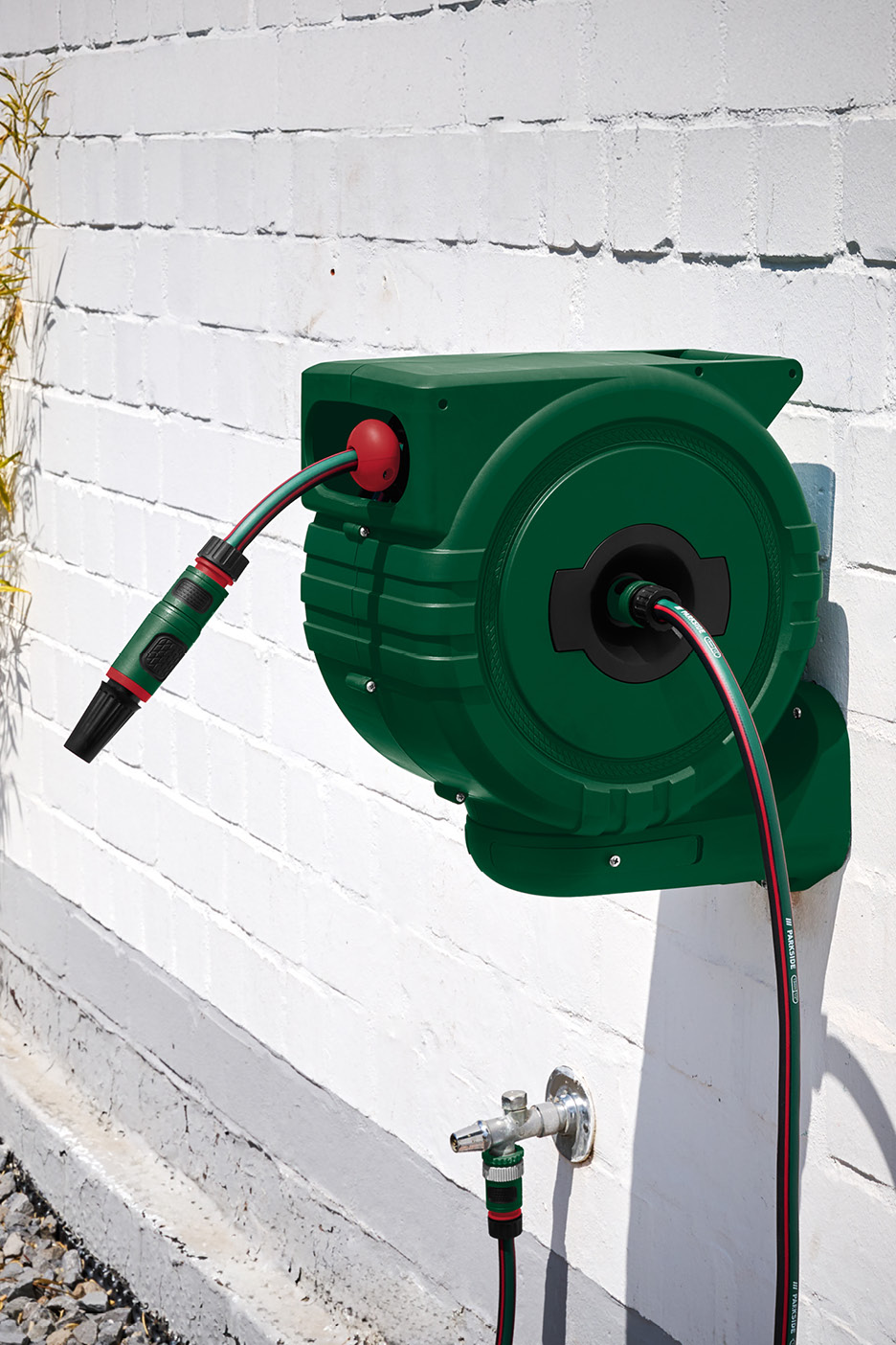 Zelený nástenný navijak na záhradnú hadicu s tryskou a pripojením na vodovodný kohútik.