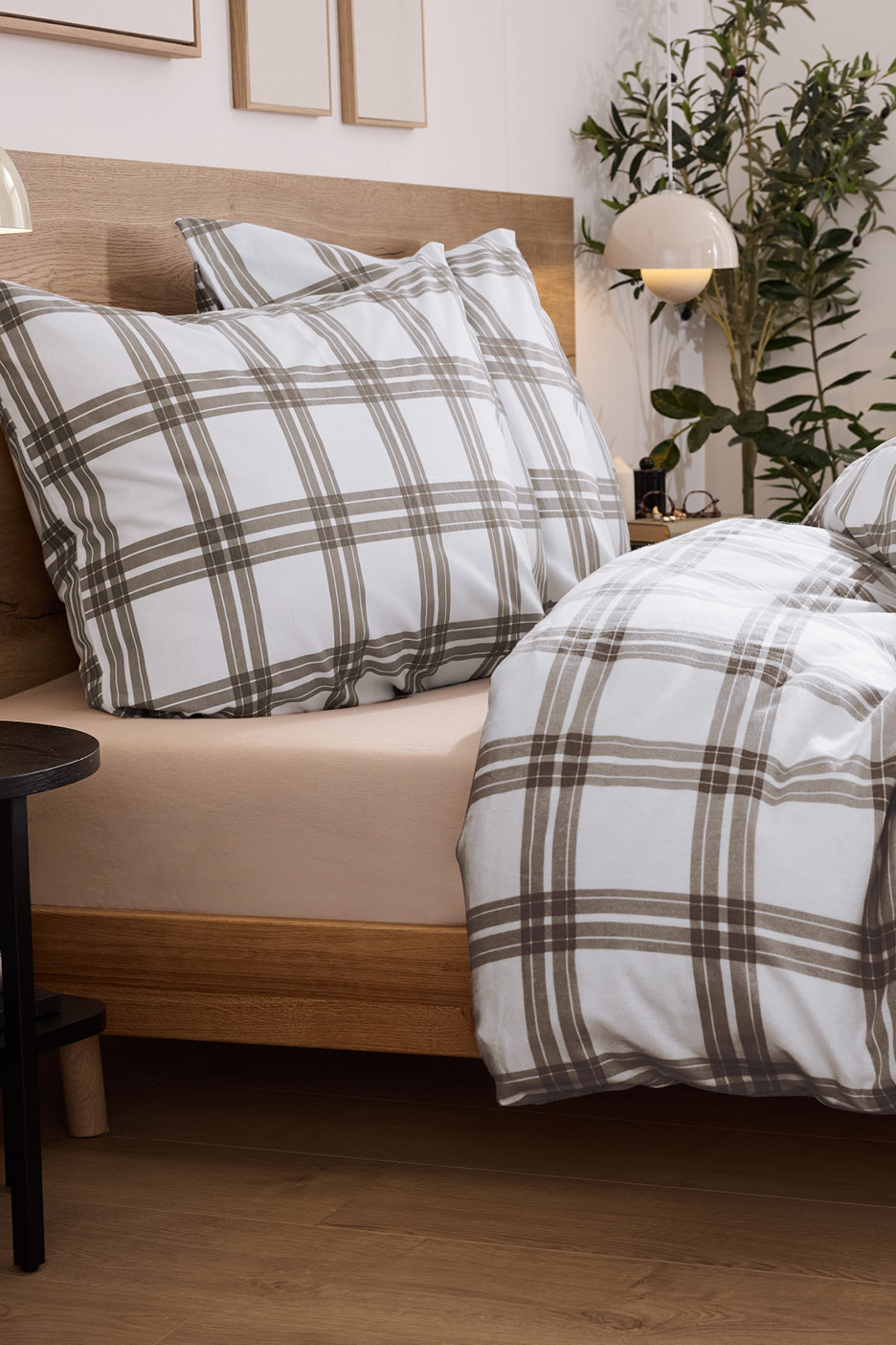 Posteľ s bielou a hnedou károvanou posteľnou bielizňou a béžovou plachtou.