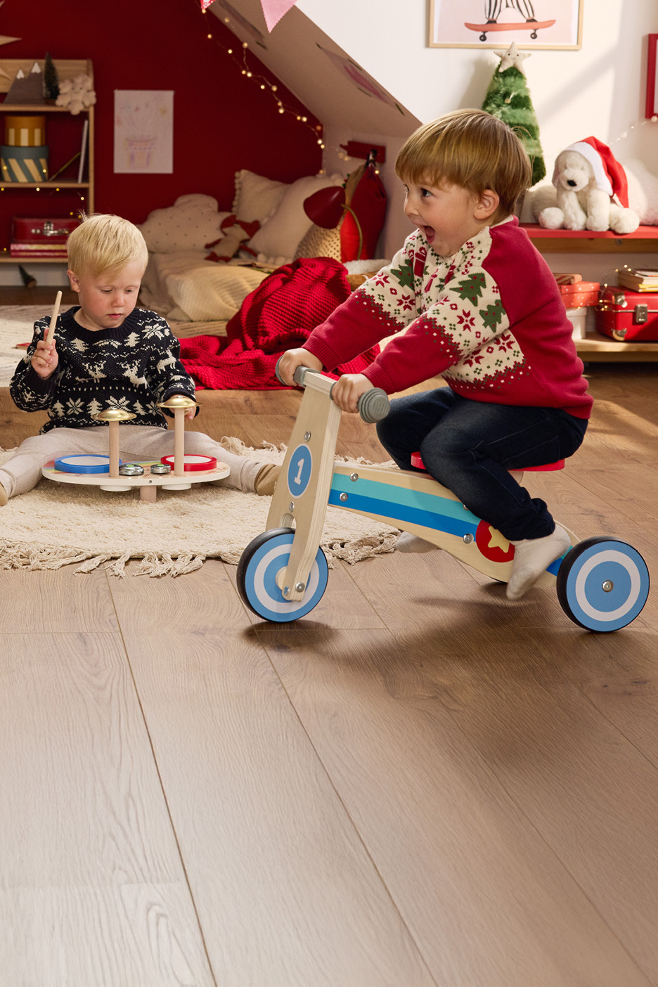 Dve deti vianočných svetroch hrajúce sa s drevenými hračkami v sviatočnej izbe.