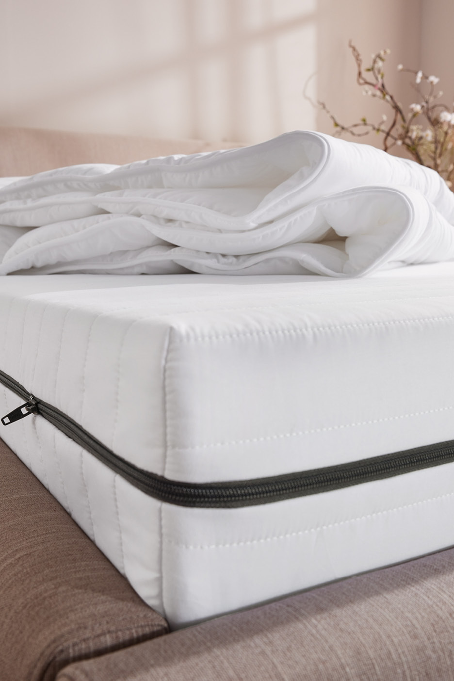 Biely matrac so zipsom a zloženou perinou na posteli.