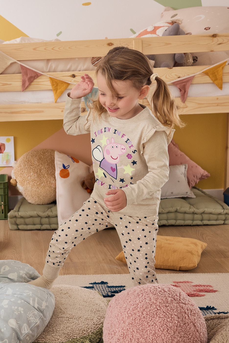 Deti v pyžamách s motívom Jurského parku a Peppy Pig sa hrajú v detskej izbe.