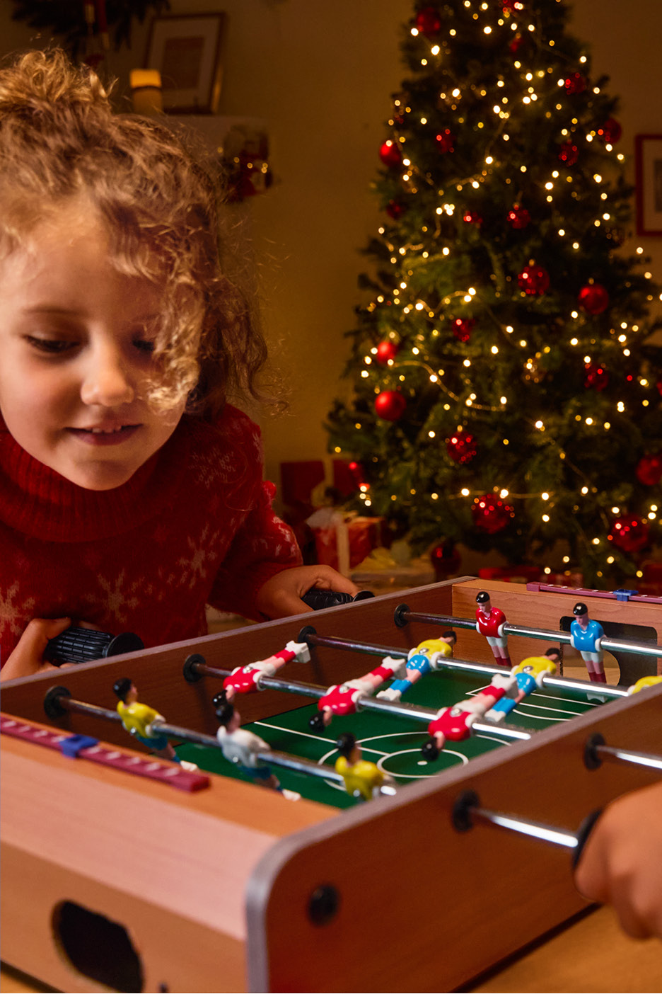 Dve deti hrajúce stolný futbal pred vianočným stromčekom.