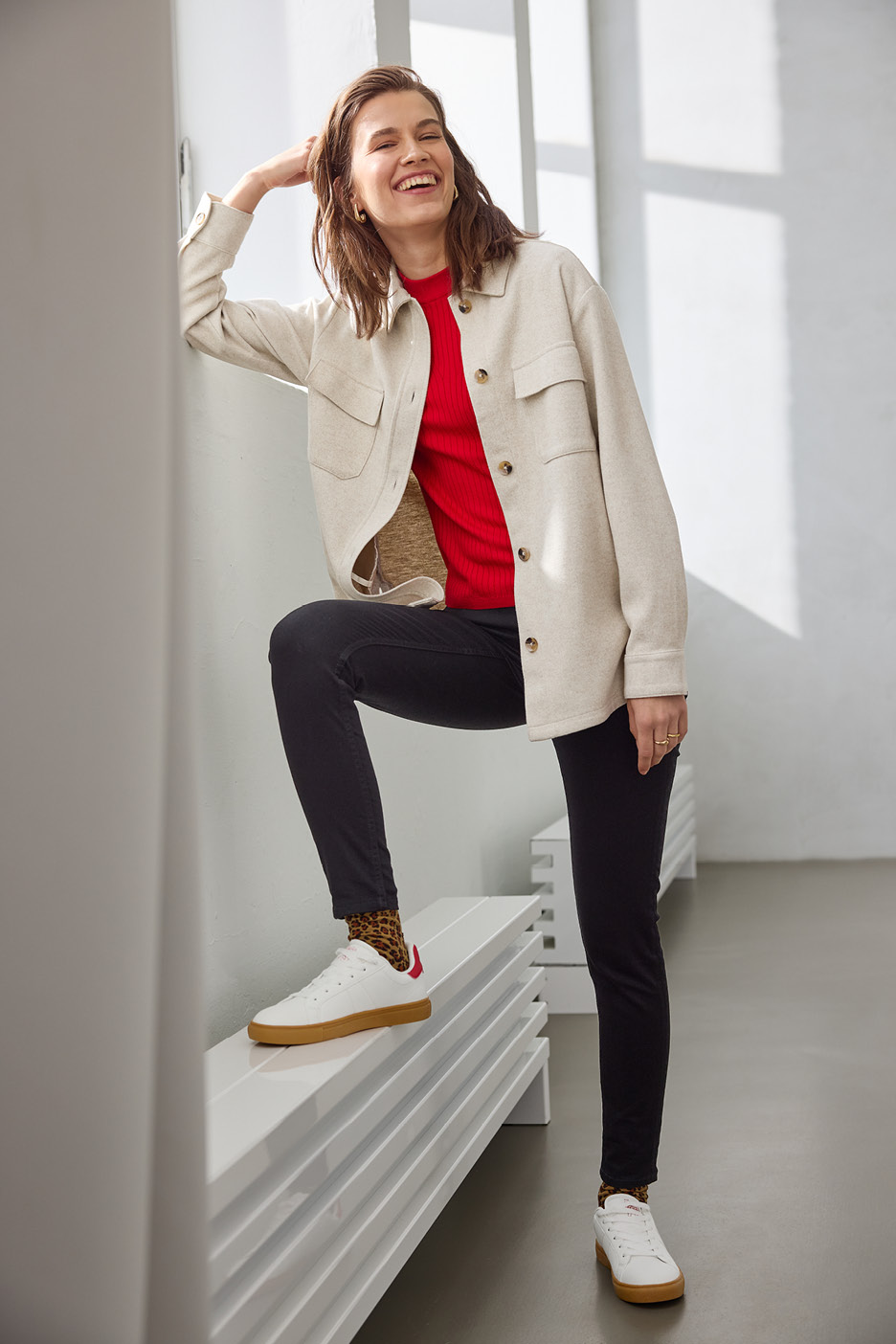 Žena v béžovej košeli, červenom tope a čiernych džínsoch s leopardími ponožkami a bielymi teniskami.