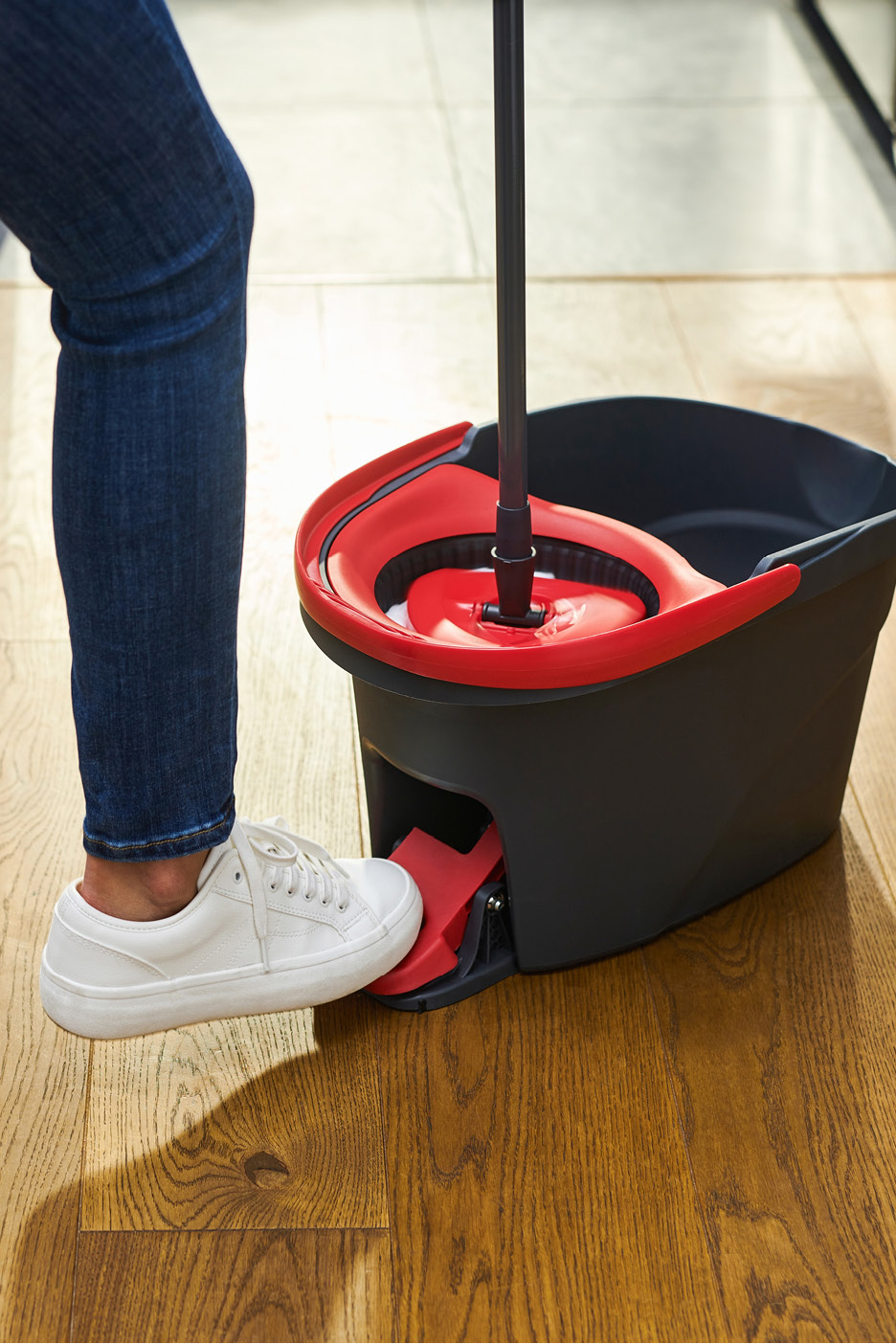 Osoba stláča pedál na vedre s mopom na odstreďovanie.