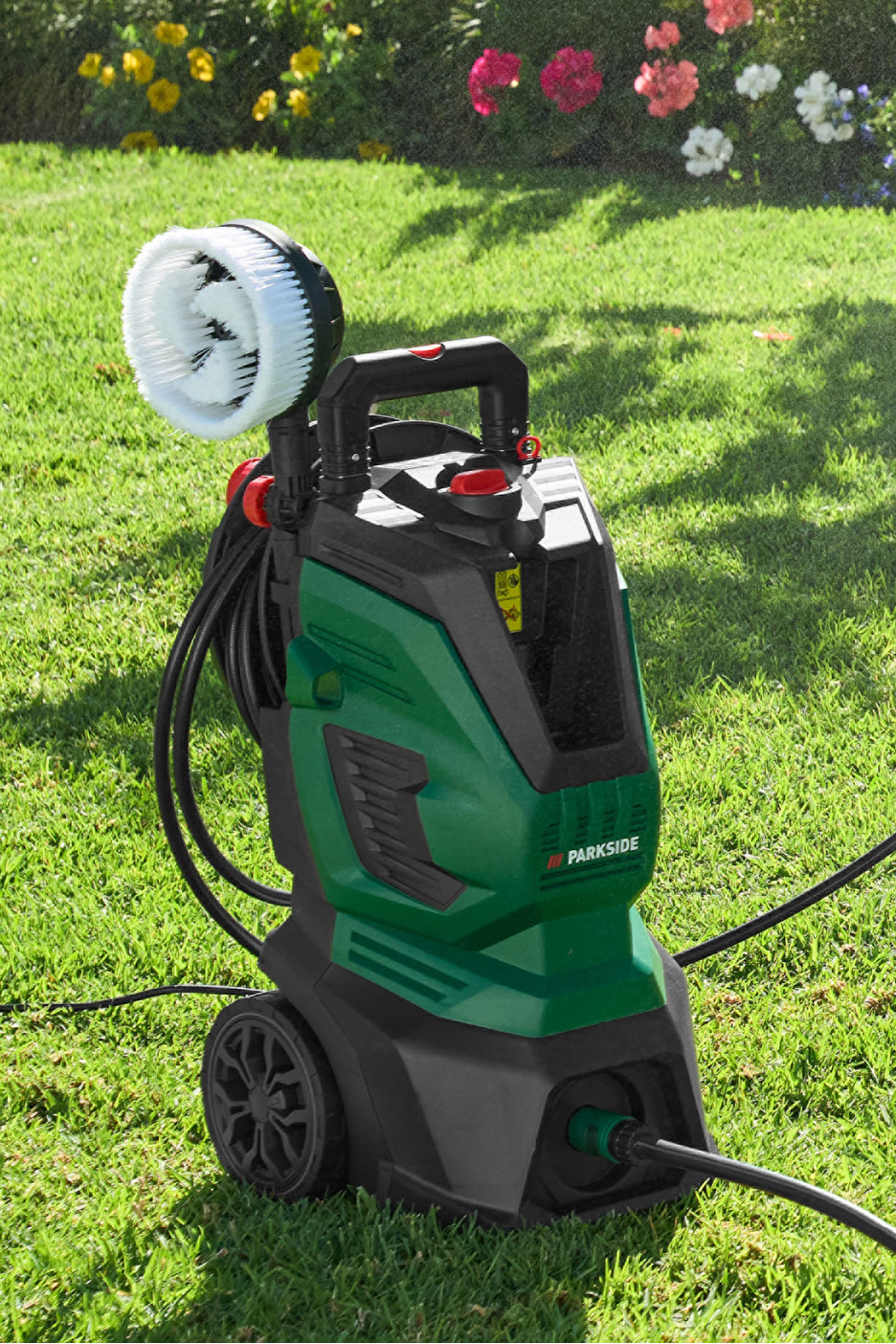 Vysokotlakový čistič s rotačnou kefou na trávniku s kvetmi v pozadí.