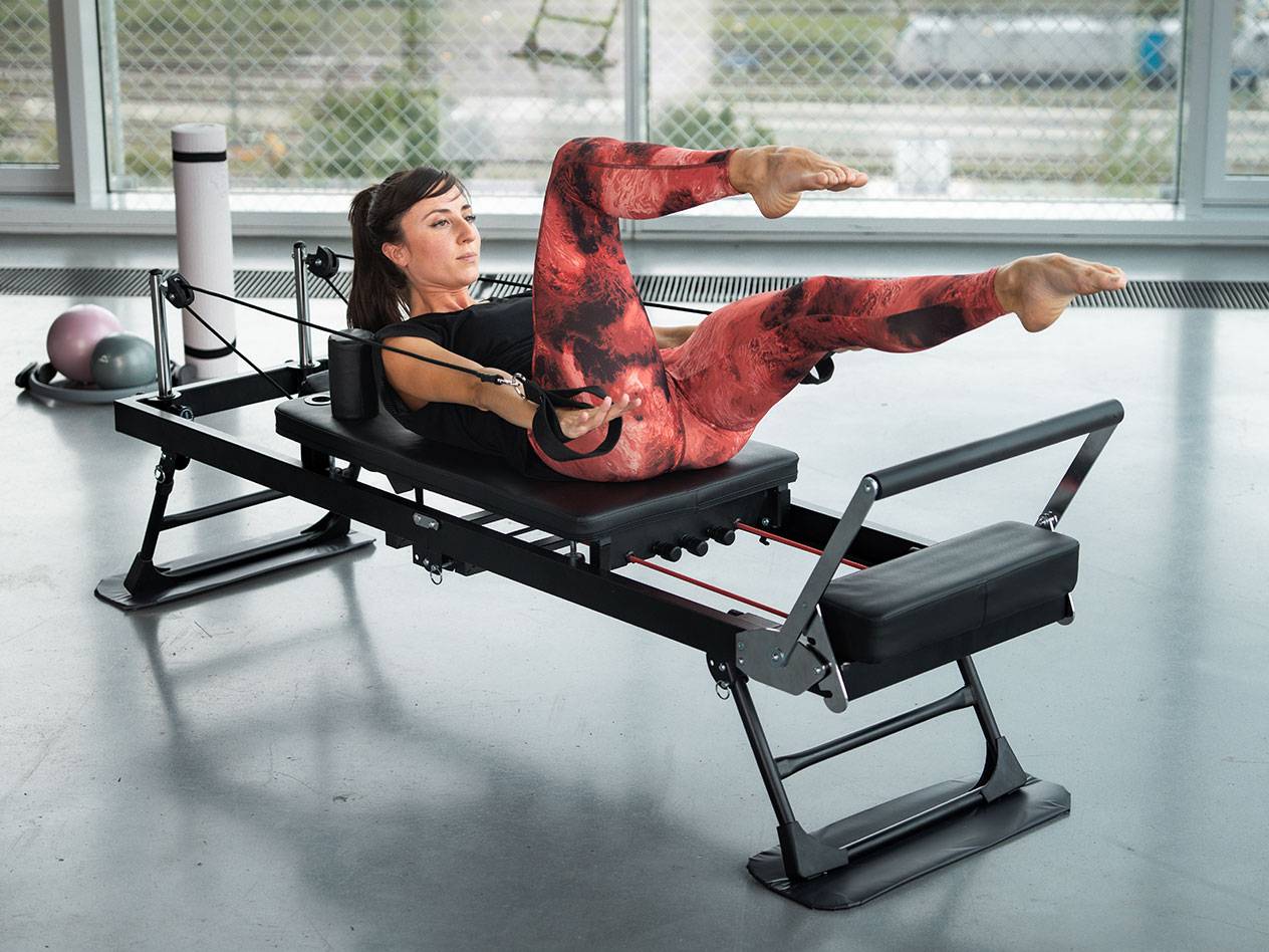 Žena cvičí Pilates na čiernom Pilates stroji s červenými detailmi.