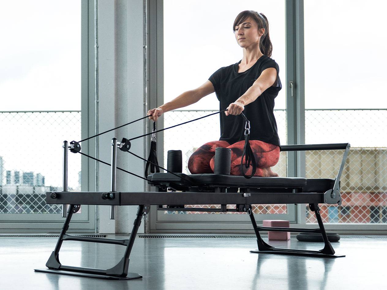 Žena cvičí Pilates na reformeri s veľkými oknami v pozadí.