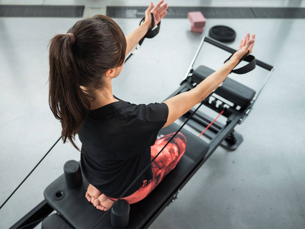 Žena cvičí Pilates na reformer stroji s odporovými pásmi.