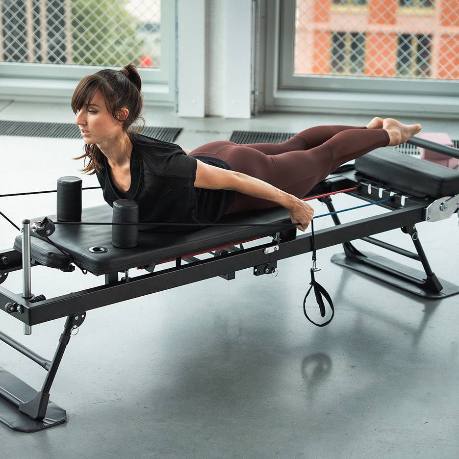 Žena cvičí na Pilates stroji s odporovými pásmi.