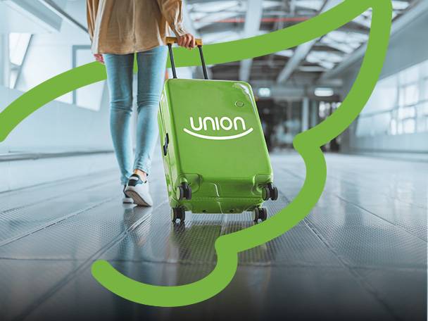 Žena ťahá zelený kufor s nápisom „union“ na letisku.