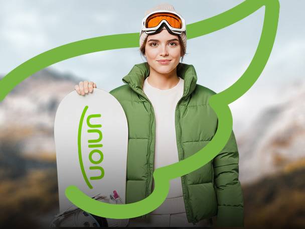 Žena v zelenej bunde a lyžiarskych okuliaroch drží snowboard s nápisom „union“.