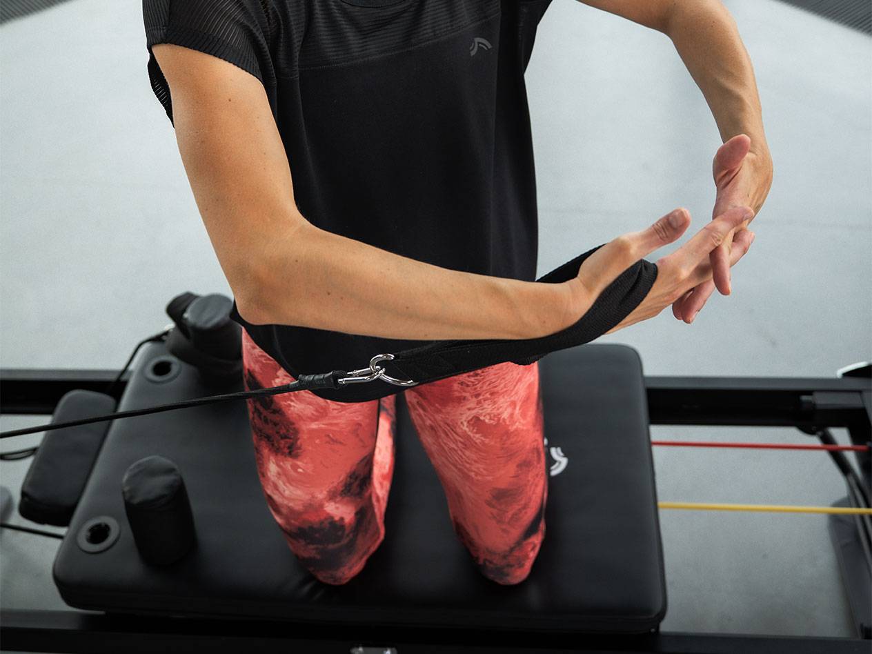 Žena cvičiaca s odporovými pásmi na Pilates stroji.