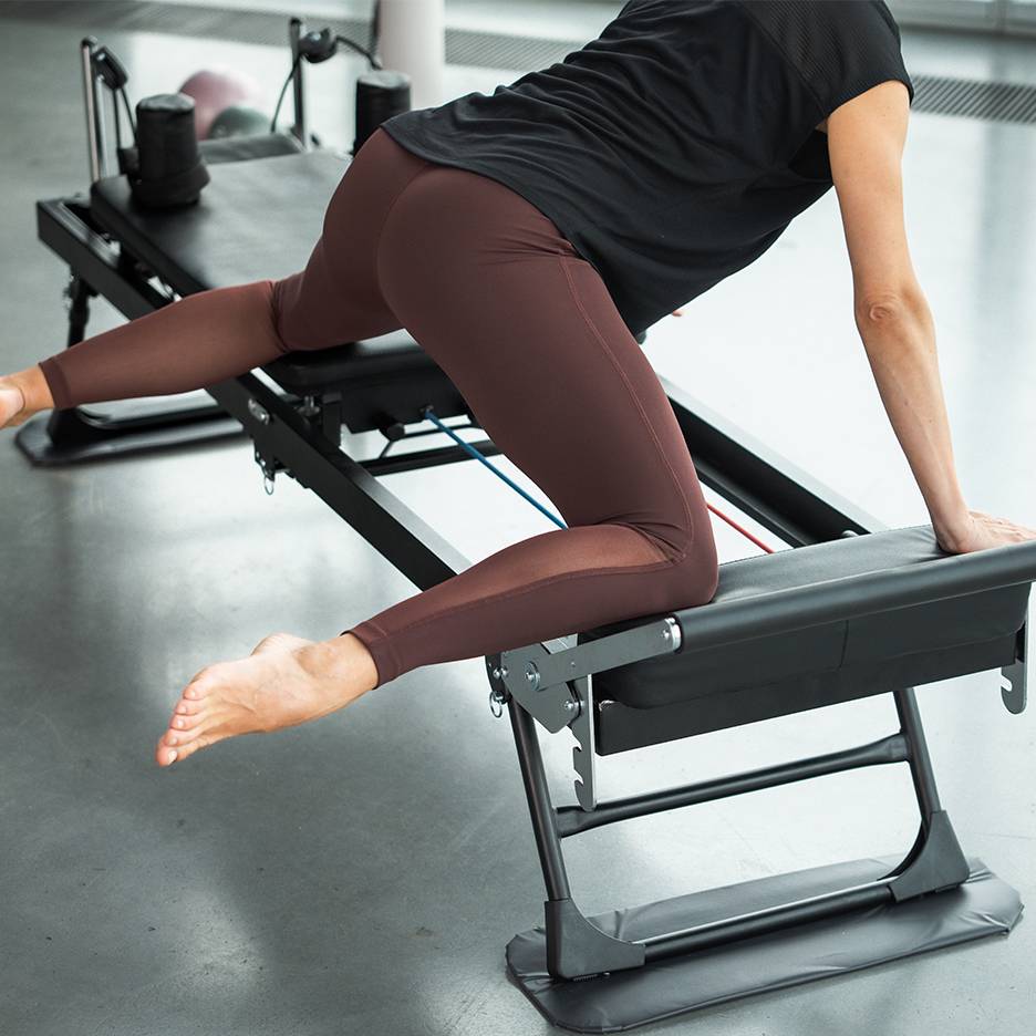 Žena cvičiaca na Pilates stroji, zameraná na nohy a zadok.