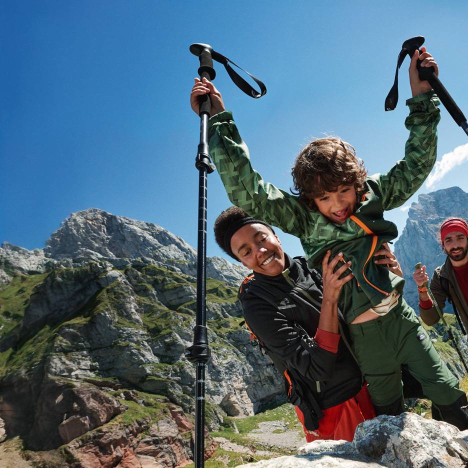 Rodina na túre s trekingovými palicami a outdoorovým oblečením v horách.