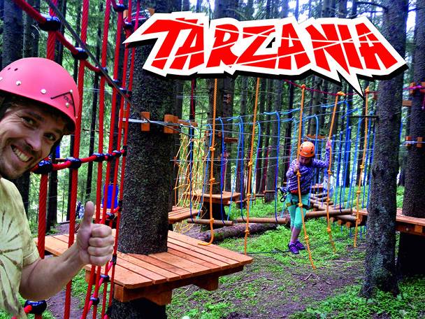 Muž a dieťa v lanovom parku s nápisom „TARZANIA“.