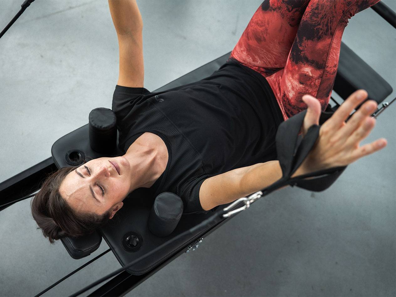 Žena v športovom oblečení leží na Pilates stroji a cvičí.