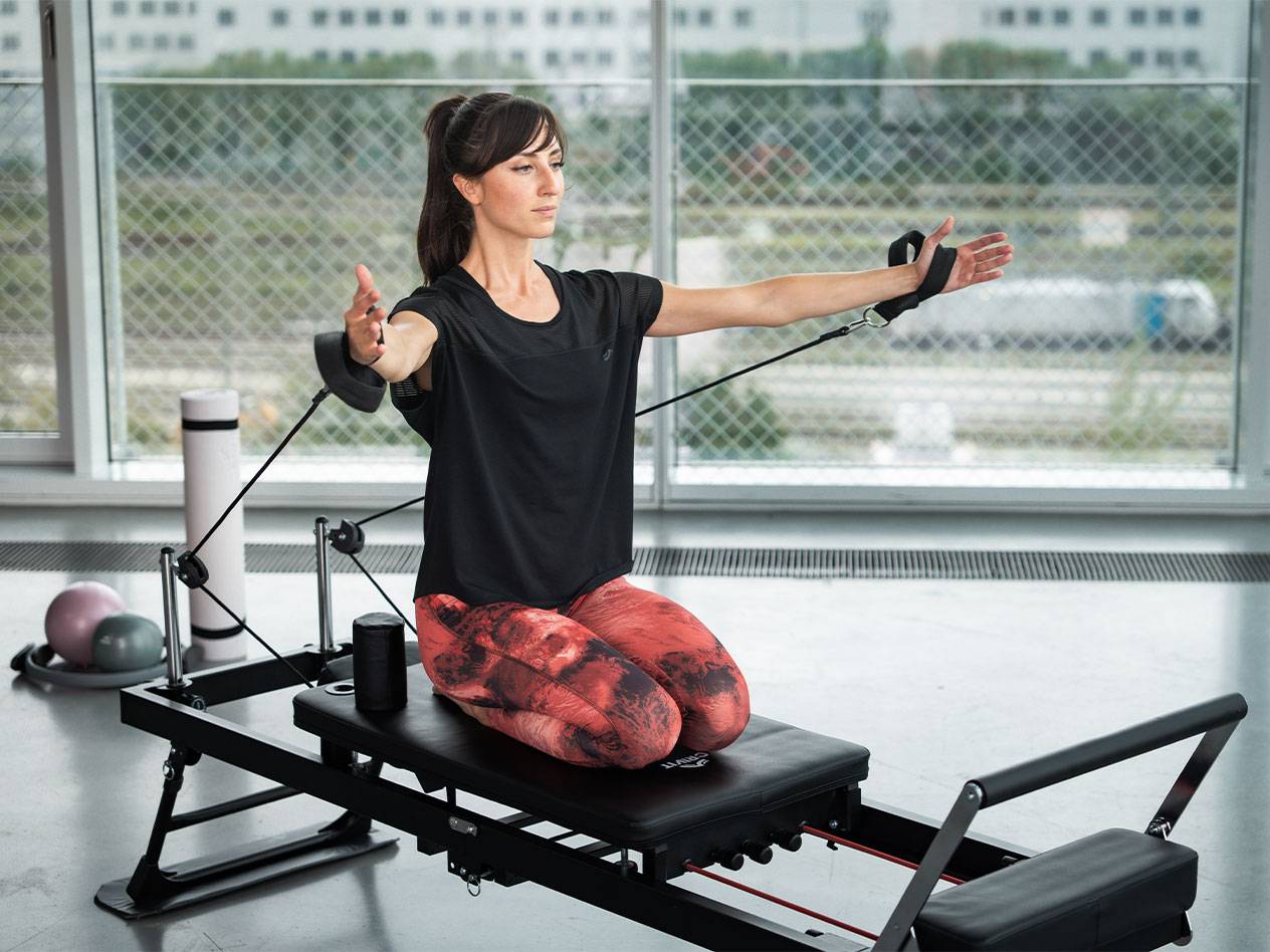 Žena cvičí Pilates na reformer stroji s odporovými pásmi.