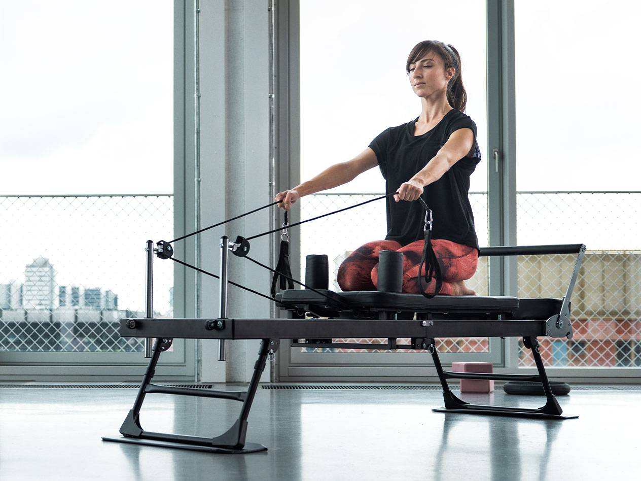 Žena cvičiaca Pilates na reformer stroji s mestským pozadím.