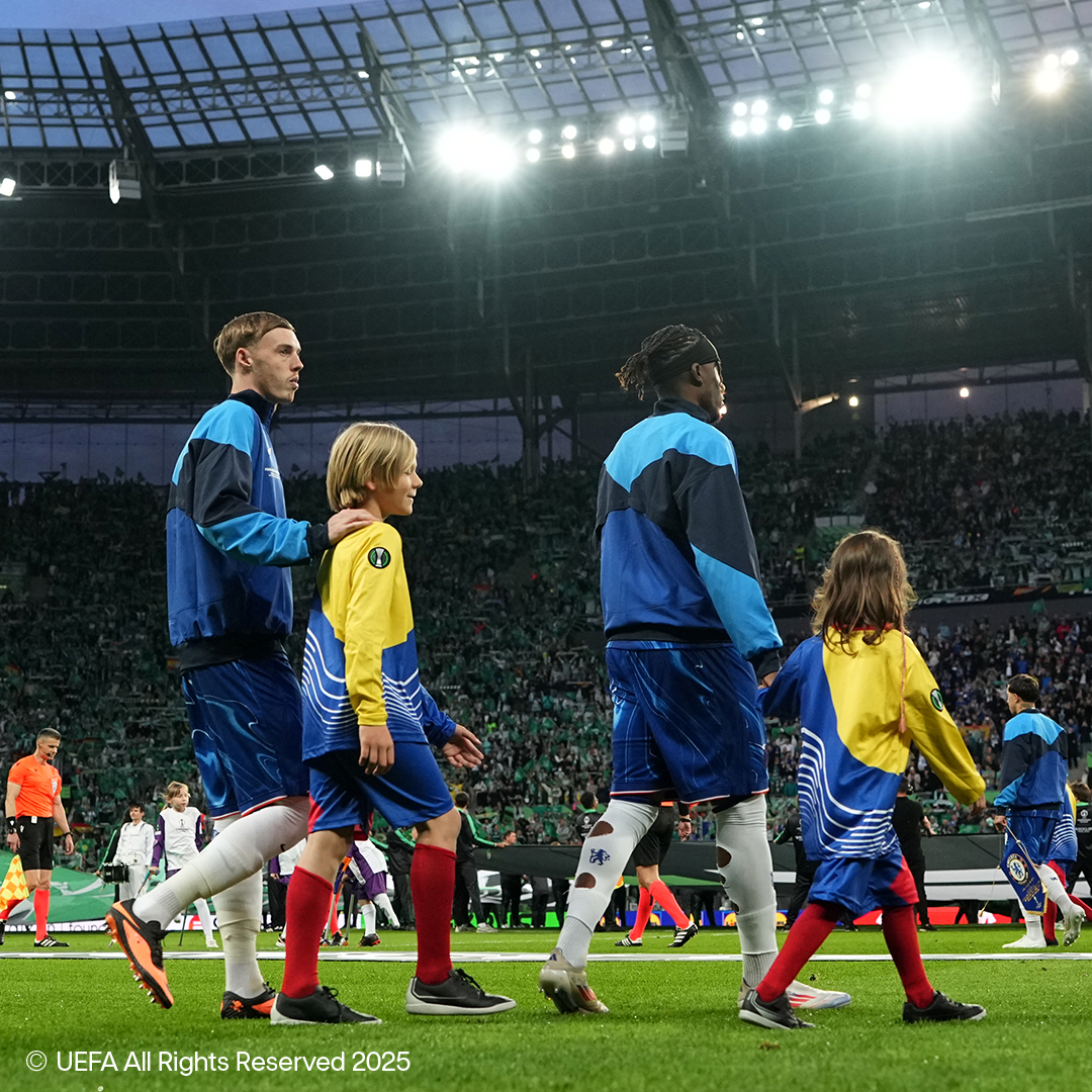 Futbalisti a deti kráčajú po ihrisku plného štadióna.
