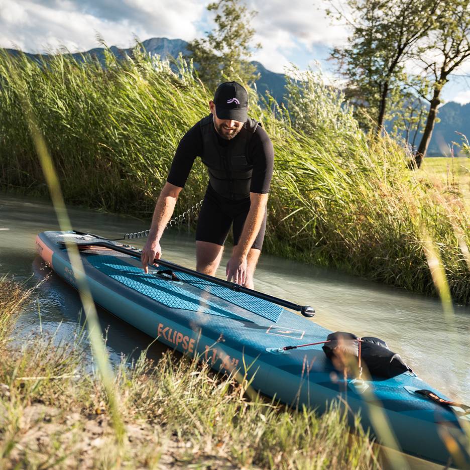 Muž v čiernom neopréne sa pripravuje na paddleboard, doska vo vode