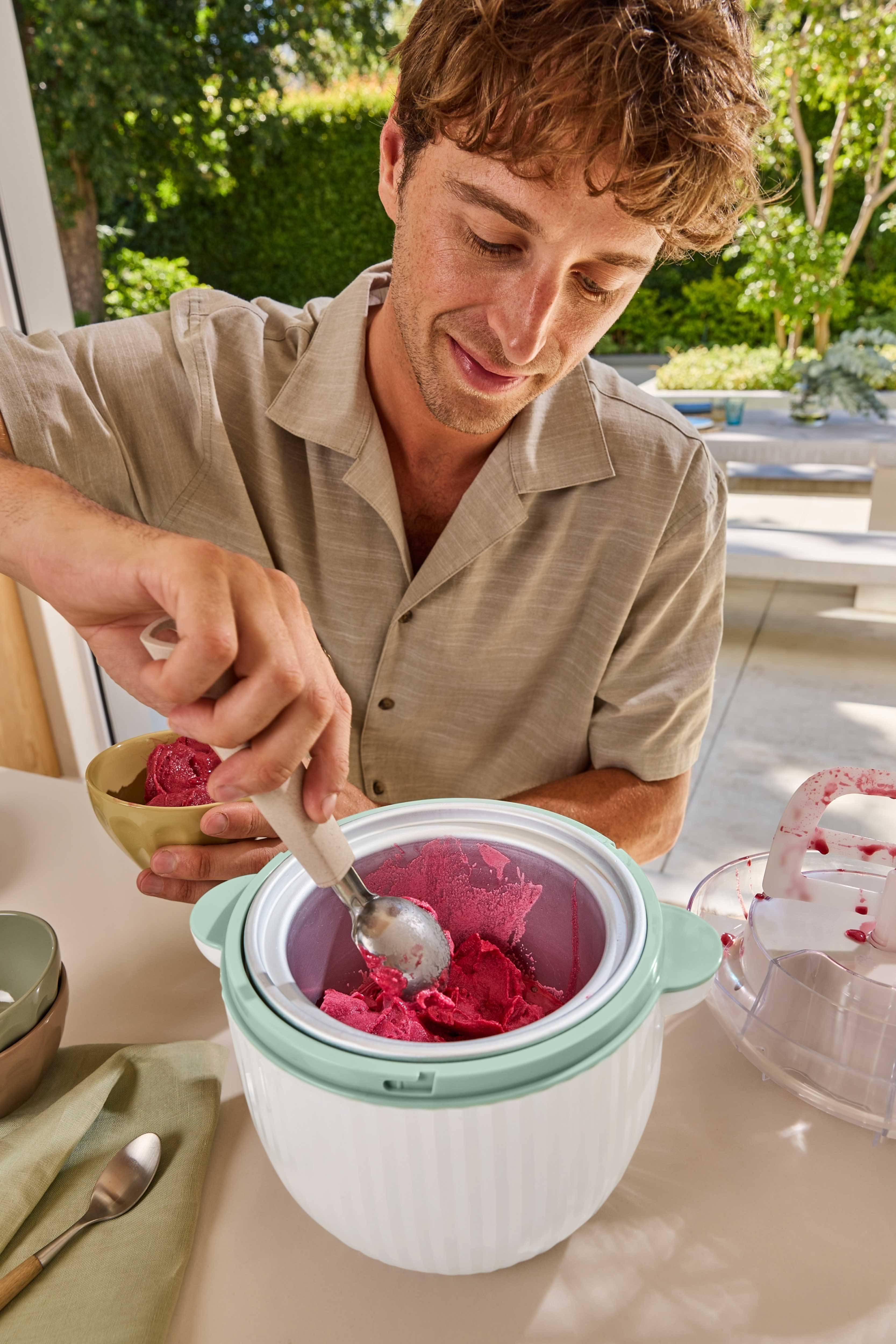 Muž naberá červený sorbet zo zmrzlinovača do misky.