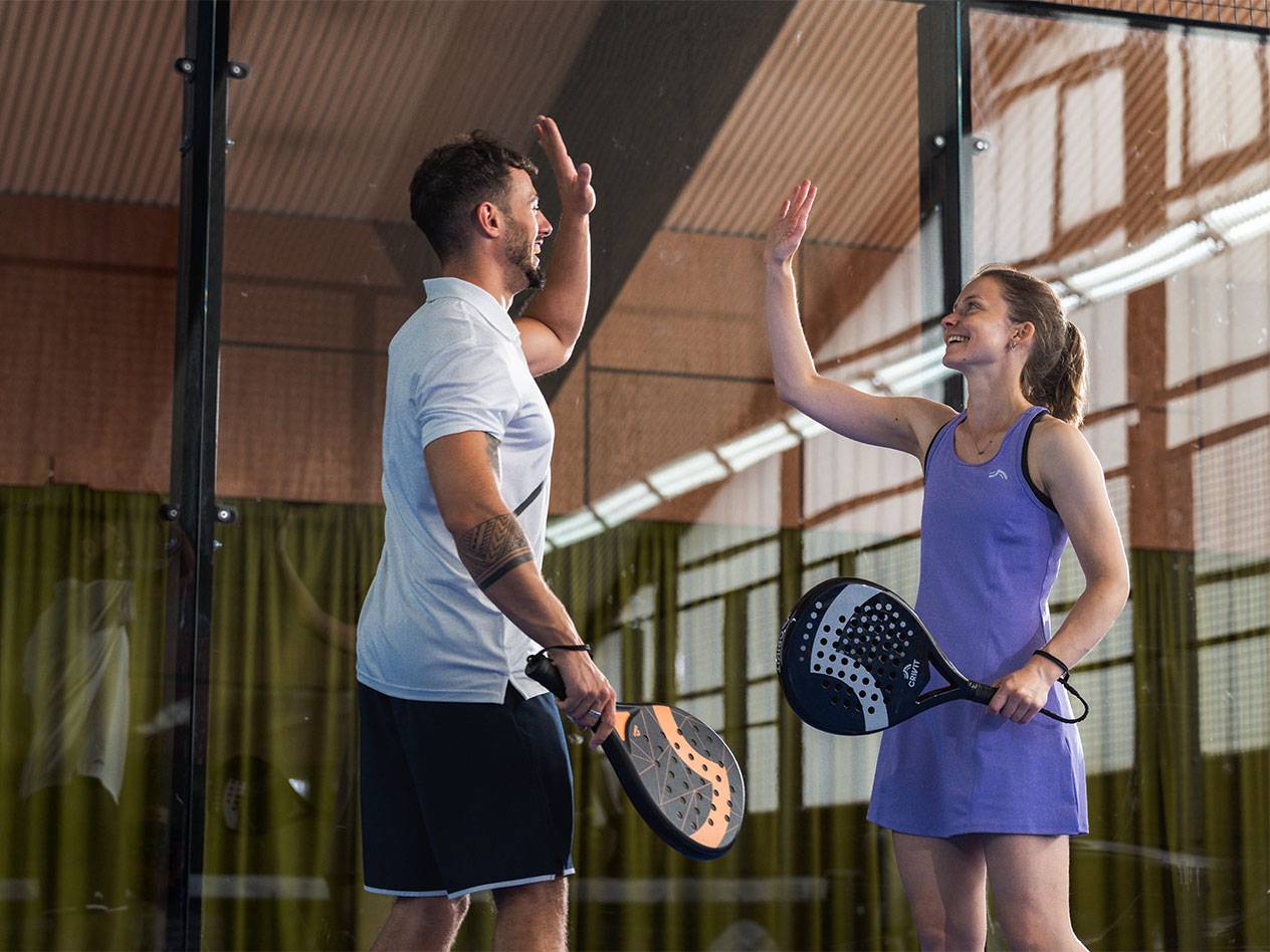 Dvaja hráči padelu, muž a žena, si dávajú high-five na kurte.