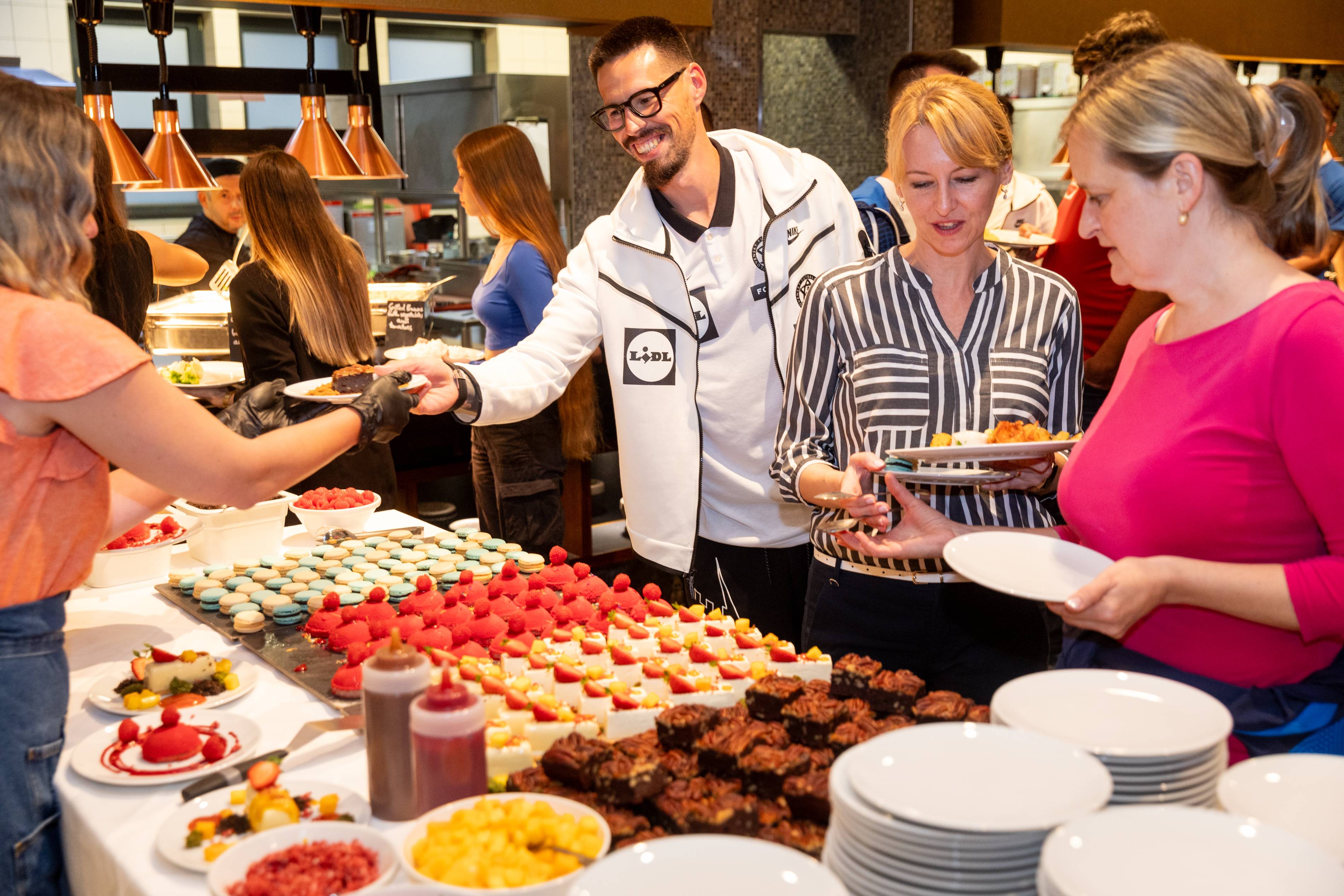 Bufet s makrónkami, koláčikmi a brownies; muž v bunde Lidl.