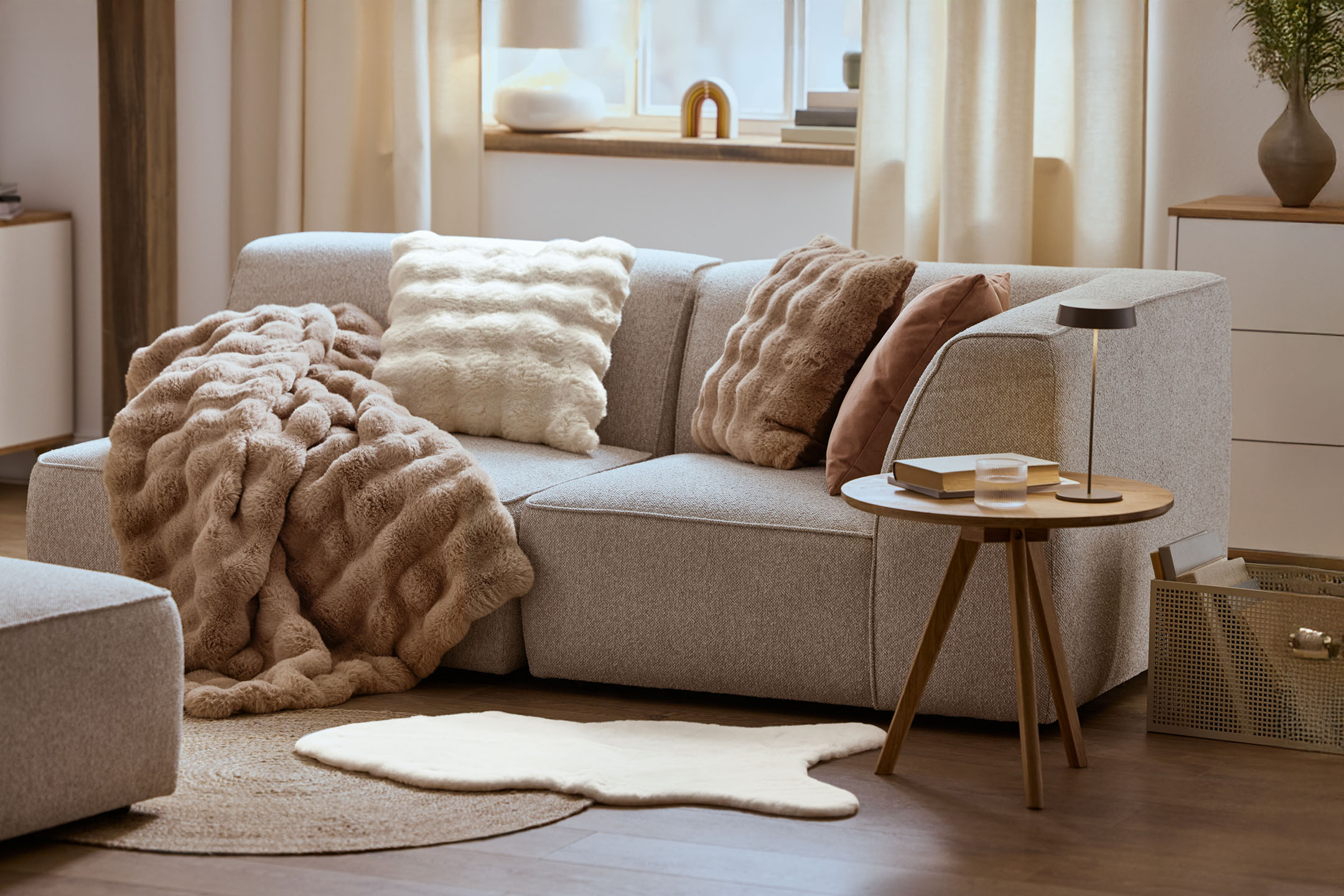 Útulná obývačka so sivou pohovkou, nadýchanými vankúšmi a dekou, dreveným konferenčným stolíkom.